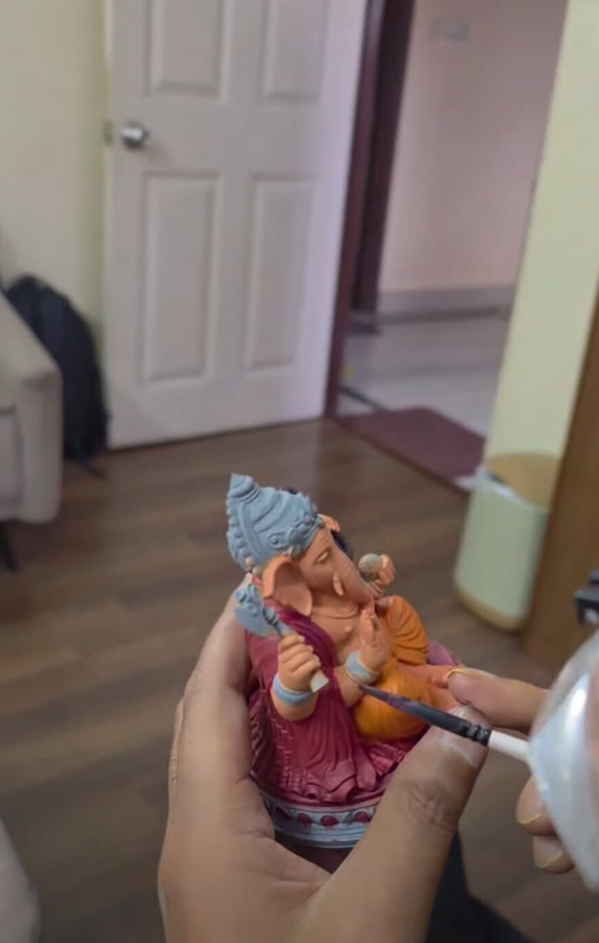 Hands holding a Ganesh statue while a fine brush picks out detail on the robes