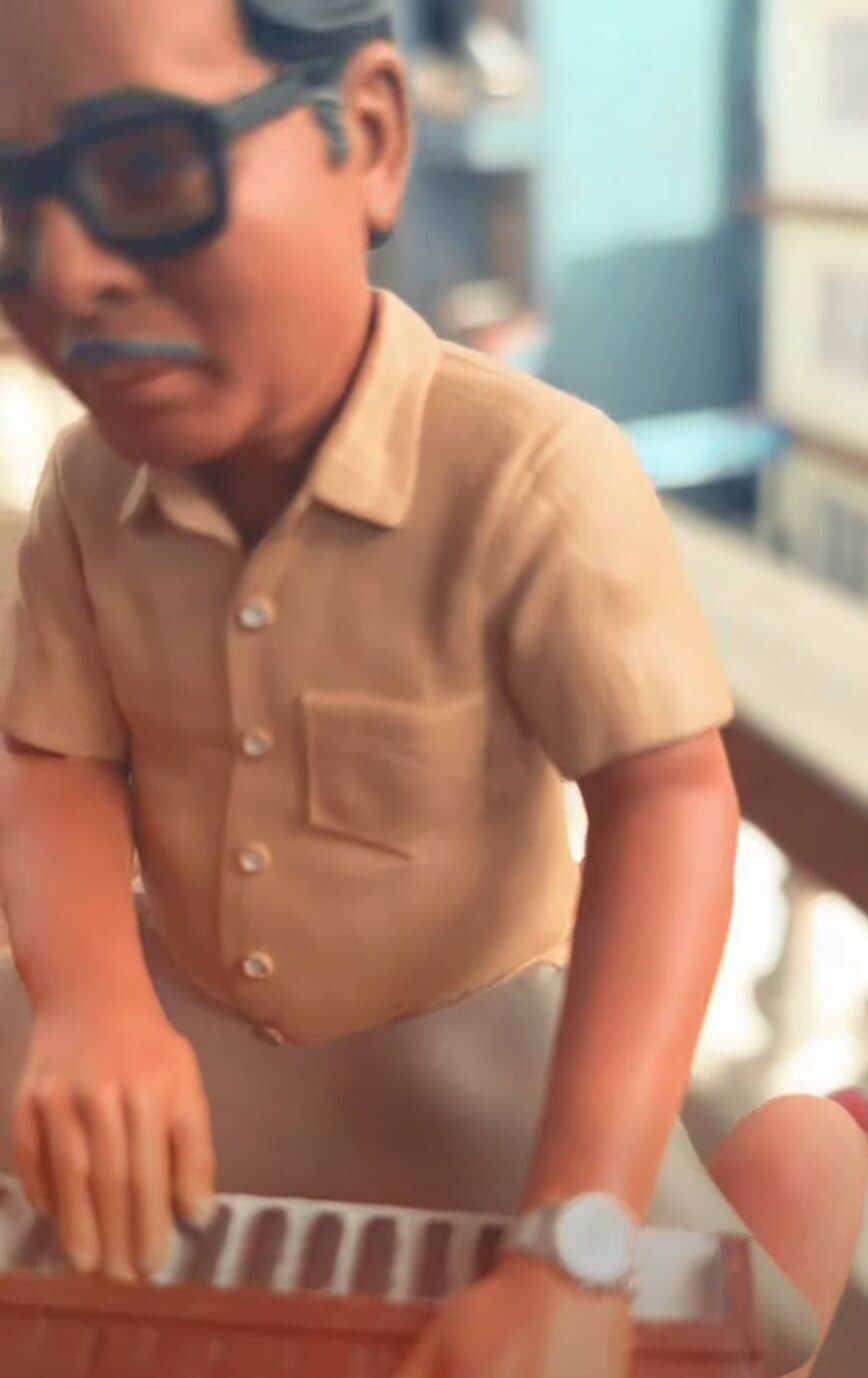 Frame from an Avatar Studios 3D animation showing a stylised character in glasses playing a harmonium
